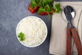 Boiled rice and cutlery in a bowl. Gray stone background.