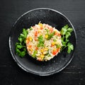 Boiled rice and vegetables. Risotto In a black plate. Top view.