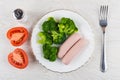 Boiled sausages with broccoli in plate, pieces of tomato, salt