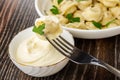 Small meat dumplings in plate, fork with dumpling on bowl with mayonnaise on wooden table