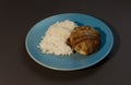 Boiled white rice with chicken cutlet wrapped in bacon on a gray background blue plate.