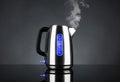 Boiling steel electric kettle with light and steam with reflection, on black background