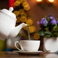 Boiling water pouring from teapot into cup. Tea ceremony with white ceramic utensils on blurred background with bokeh Royalty Free Stock Photo