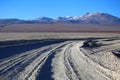 A dusty road with dark soil crossing the desert and mountains in the background. Adventure in Bolivia highlands. Royalty Free Stock Photo