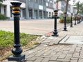 A row of decorative, black metal bollards with distinct yellow-orange bands lining a paved pedestrian walkway or sidewalk. Royalty Free Stock Photo