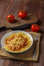 Bolognese pasta in a plate on a wooden round stand next to tomatoes on a wooden board