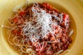 Bolognese pasta sprinkled with grated parmesan in yellow deep plate, selective focus