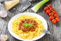Bolognese ragout with italian pasta on a white plate, decorated with basil leaves, authentic recipe, wooden background with celery