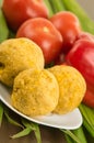 Bolon, an ecuadorian typical food on a white plate with a blurred tomato and pepper behind, over a green leaf