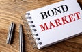 BOND MARKET text on notebook with pen on wooden background