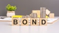 BOND text on wooden cube blocks with coins above. above suggests a focus on investment in bonds, financial stability