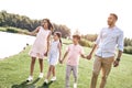 Bonding. Family of four walking on a grassy field near lake hold Royalty Free Stock Photo