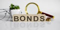 BONDS concept on wooden cubes and flower ,glasses ,coins and magnifier on the white background Royalty Free Stock Photo