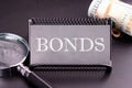 BONDS text on the business card next to the money, a magnifying glass on a black background Royalty Free Stock Photo