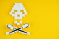 The bones skull made of sugar cubes and dessert spoons on a yellow background. Sugar kills and diabetes concept