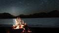 a bonfire burns at night against the background of mountains and sea with bright stars.. Royalty Free Stock Photo
