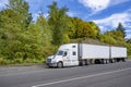 Bonnet big rig white semi truck with high cab and two dry van semi trailers standing out of service on road shoulder with green