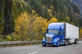 Bonnet blue big rig semi truck tractor carry cargo in refrigerated semi trailer driving on the autumn highway road with rock Royalty Free Stock Photo