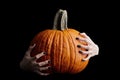 Bony hands holding halloween pumpkin on black background