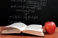 Book and Apple on wooden table in front of blackboard where is mathematical equation in the classroom Royalty Free Stock Photo