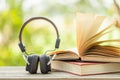 Book and black headphone on wooden table with abstract green nature blur background. Reading and education concept Royalty Free Stock Photo