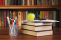 Stack of books on a desk with an apple and an organizer for pens Royalty Free Stock Photo