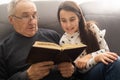 Book, family and children with a girl reading to her grandfather on the floor of their living at home. Kids, read and Royalty Free Stock Photo