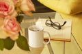 Book, glasses, roses and a mug with tea on modern glass table. Living room interior home decor concept