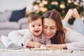 With book that is on the ground. Mother with her little daughter is indoors at home together Royalty Free Stock Photo