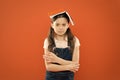 Book on her head. Little girl book roof head. Small girl book orange background. Interesting story for kid. Studying and