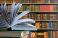 Book in library with old open textbook, stack piles of literature text archive on reading desk, and aisle of bookshelves in school