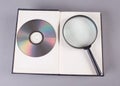 Book with magnifying glass, compact disk on grey
