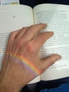 book reading. Left hand on top of the pages with rainbow light falling on the wrist.