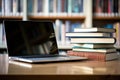 Book stack and laptop computer on a desk in library room with blurred bookshelf background