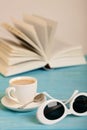 Book, sunglasses and cup of coffee on a wooden blue background.