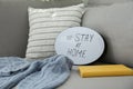 Book, sweater and speech bubble with hashtag STAY AT HOME on sofa, closeup. Message to promote self-isolation during COVIDÃ¢â¬â19 Royalty Free Stock Photo