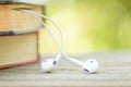 Book and white earphone on wooden table with abstract green nature blur background. Reading and education concept