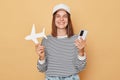 Booking an economy flight. Flying around the world. Smiling woman wearing baseball cap and striped shirt holding white paper plane