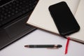 A bookmarked notebook, cell phone, pen, and laptop computer on a white desktop. Royalty Free Stock Photo