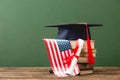 Books, academic cap, diploma and american flag on wooden surface Royalty Free Stock Photo