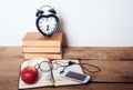 Books, alarm clock, notepad, cellphone with earphones and apple on wooden background