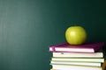 Books and apple near green chalkboard. School education Royalty Free Stock Photo