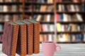 Books backgrounds. Closeup of antique books with a coffee mug on a wooden table over abstract blurred bookshelf in library. Royalty Free Stock Photo