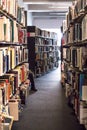 Books on library shelves with leg of person visible further down the isle. Modern building