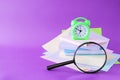 Books, magnifying glass, alarm clock and notepads, pastel colored paper, on the table, purple background