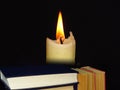 Books stacked in a pile and a candle on black background. Royalty Free Stock Photo