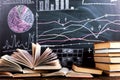 Books on the table against the background of a chalkboard on which are drawn graphs and charts of growth and decline. Business