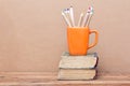 Books tower and orange mug with colored pencils