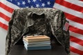 Books, watch and soldier uniform on chair near flag of United States. Military education