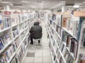 Bookshelves with books, bookshelves in bookstore. Unrecognizable man, back to us sitting on a chair and reading a book Royalty Free Stock Photo